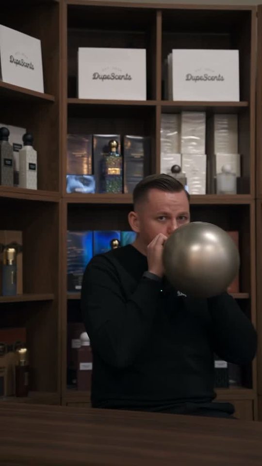 Stillbild ur reel: en man blåser upp en ballong framför parfymhyllorna i Dupescents butik.